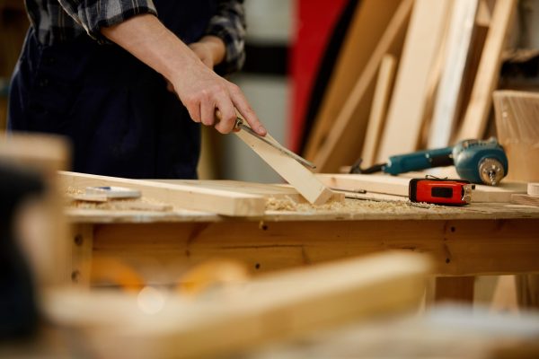 Closeup of unrecognizable carpenter carving wood while working in joinery lit by sunlight, copy space